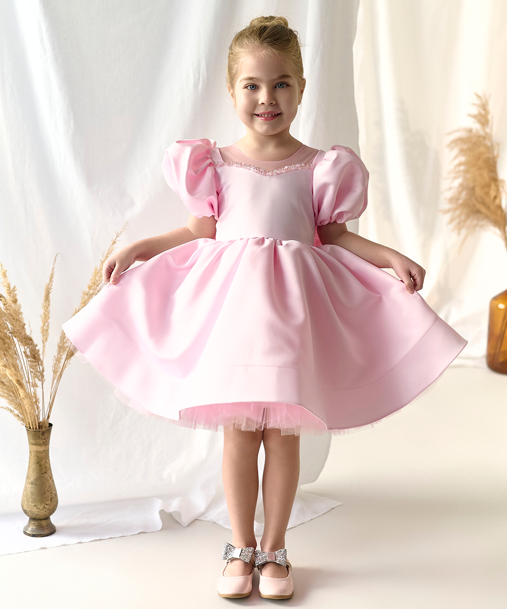 A young girl holding out the skirt of a deep burgundy velvet dress trimmed with white lace